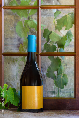 Bottiglia di vino senza etichetta sul davanzale con foglie di vite e finestra in legno