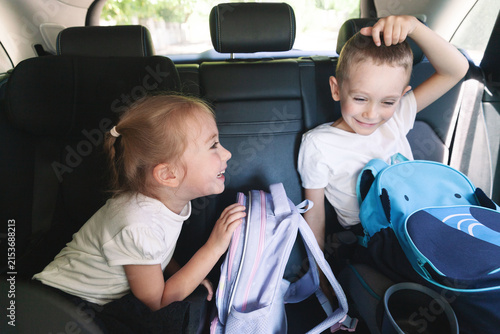 Smiling brother and sister with school backpacks sit in a car, excited for their first day of school and a new learning adventure