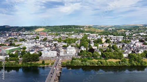 Luftbild von Trier mit der antiken Römerbrücke über die Mosel, umgeben von Stadtarchitektur und grünen Hügeln unter bewölktem Himmel an einem Sommertag.