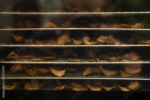 Drying pear slices in a dehydrator. A view of the wire shelves with sliced ​​fruit through the glass door.