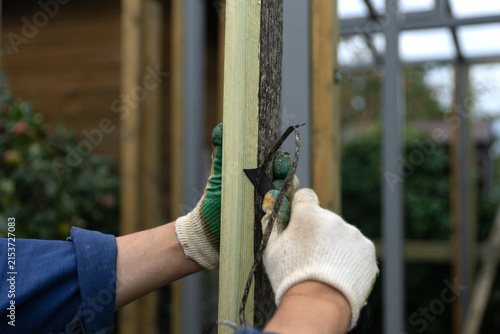 Attaching wood to a metal structure through a layer of roofing felt, which acts as a waterproofing and damping agent. Men's hands trim off excess roofing felt attached to the lumber.