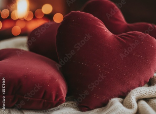 Close-up of red velvet heart-shaped pillows on a cozy knitted blanket with warm bokeh lights in the background, symbolizing love and comfort, concept of love and comfort