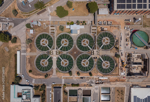 Overhead view of eight circular flocculation-decantation clarifiers at an industrial drinking water treatment facility, surrounded by roads, solar panels and infrastructure