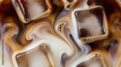 Top view macro of iced coffee with melting ice cubes, white milk swirling into dark brown liquid, refreshing cold drink texture with bubbles.