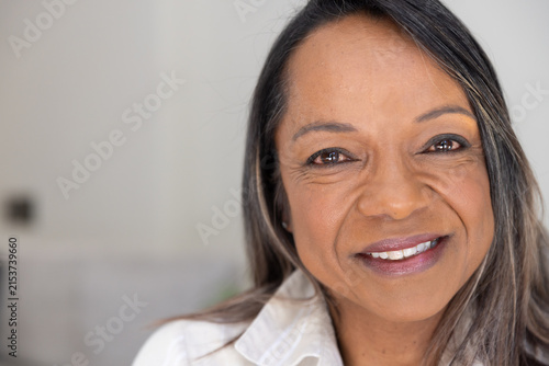 Mature African American woman smiling, wearing collared shirt in neutral room with outlet visible