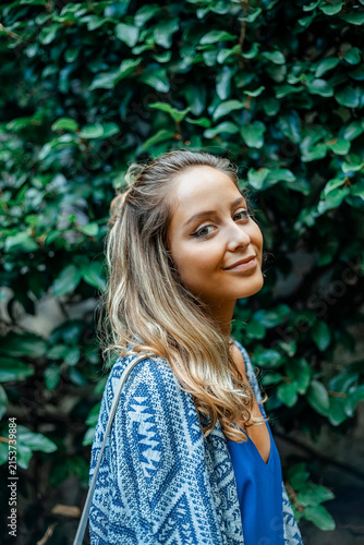 Portrait of Smiling Young Woman Outdoors Standing Near Green Hedge