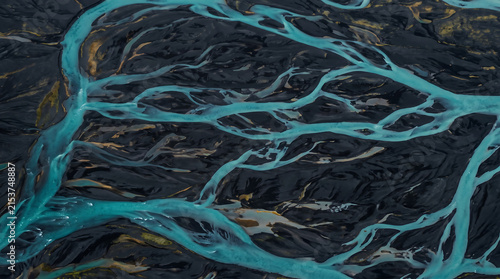 Aerial view of a glacial river system winding through black volcanic sand and rock formations in Icelands highlands