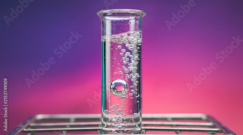 Close up of a clear glass test tube filled with bubbling liquid against a vibrant purple and pink gradient background