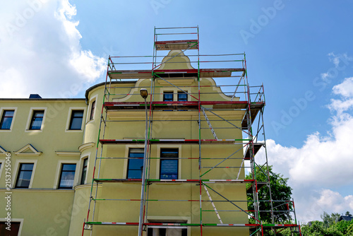 Bild auf Leinwand Metal scaffolding structure installed on the exterior facade of a classic yellow building for reconstruction and painting against a blue sky with clouds
