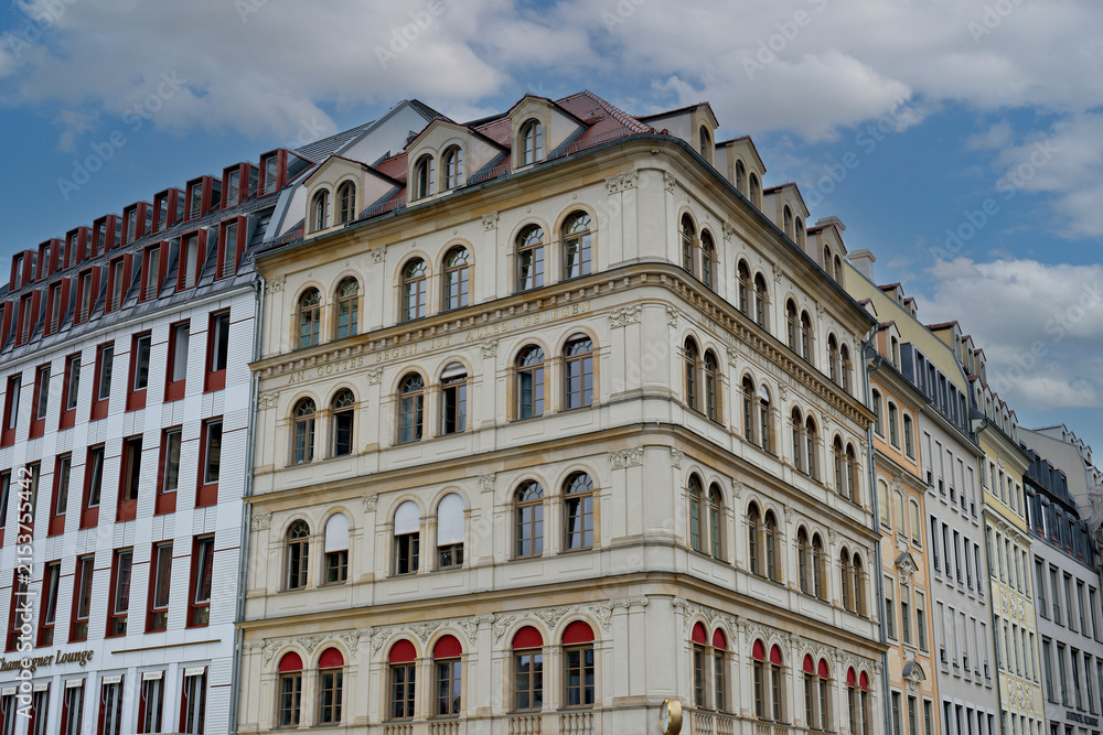Obraz premium Low angle view of a beautiful historic European building with an ornate beige facade, arched windows, and red awnings under a cloudy sky.