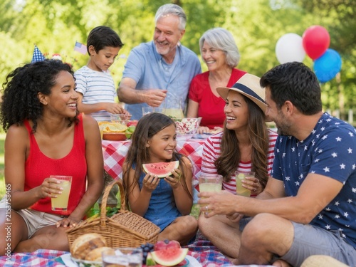 Mehrgenerationenfamilie und Freunde feiern Labor Day bei einem fröhlichen Picknick im Park mit sommerlichem Essen, Getränken und entspannter gemeinsamer Zeit im Grünen.