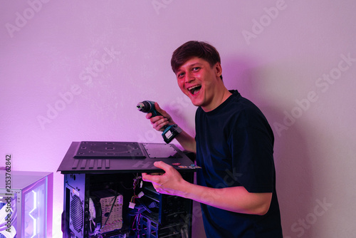 Man laughing excitedly while holding cordless drill, assembling or customizing high performance gaming desktop computer with visible internal component setup.