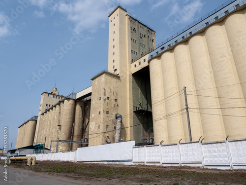Large concrete grain elevator building against a clear blue sky, industrial agricultural storage facility for grain processing and farming
