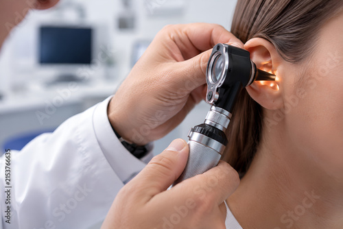 Macro shot of an ENT doctor's hands using a lighted medical otoscope to examine a patient's ear canal