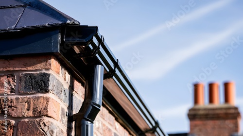 Black guttering and downpipe on a brick house roofline exterior detail