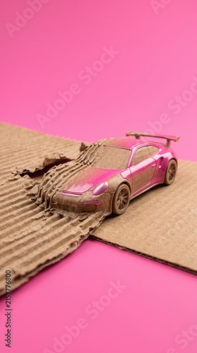 Miniature pink sports car emerging from corrugated cardboard packaging. Creative logistics and fast e commerce delivery concept on bright pink background.
