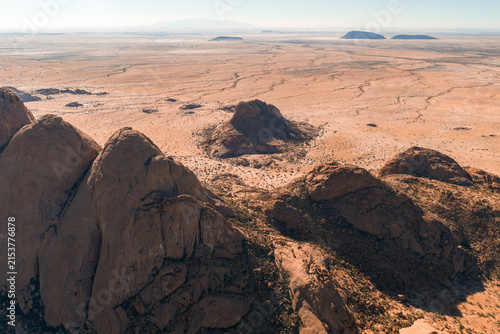 Принти на полотні An aerial perspective shows massive granite peaks rising from the expansive arid plains of the Namib desert landscape in Namibia under a clear sky