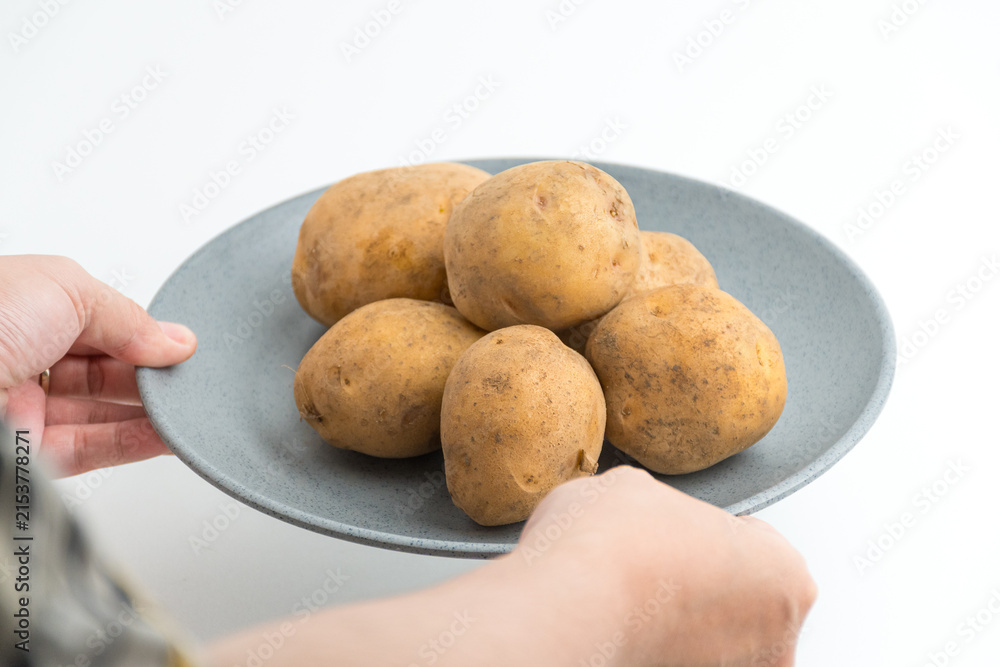 Fototapeta premium Hands holding and arranging fresh raw baby potatoes on grey ceramic plate isolated on white