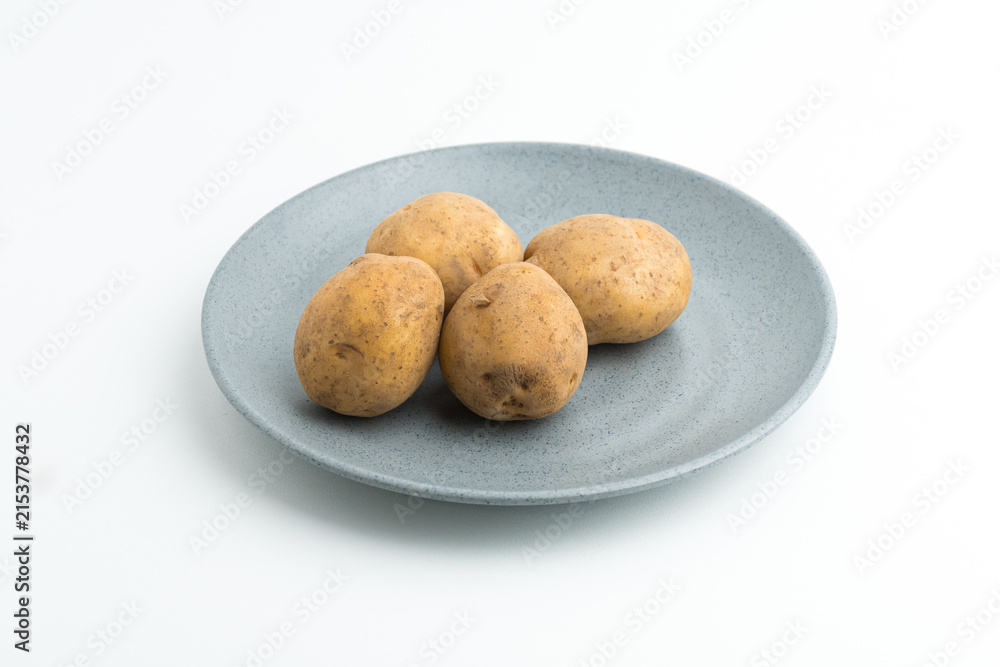 Fototapeta premium Fresh raw baby potatoes served on a grey ceramic plate isolated on white background