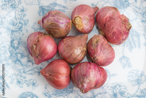 Fotografie Fresh red onions shallots served on a blue patterned ceramic plate isolated on w