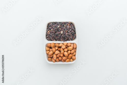 Raw red peanuts and black beans in a white divided ceramic dish on white background