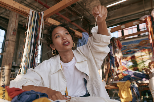 Young woman artisan holding a needle and thread while working on a textile project in a studio