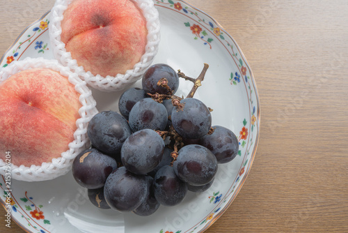 Foto Fresh peaches and dark grapes rest on a floral plate atop a wooden table with ample copy space