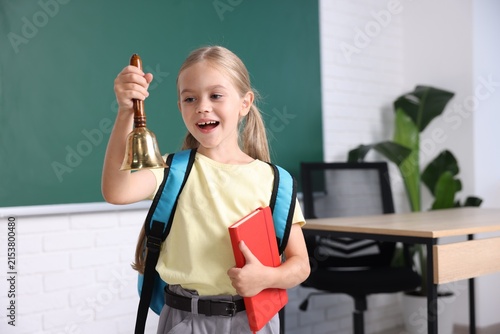 Pretty little girl with school bell and notebook in classroom