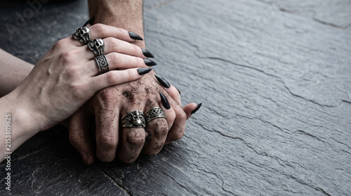 Two contrasting entwined hands with dirt and gothic silver rings