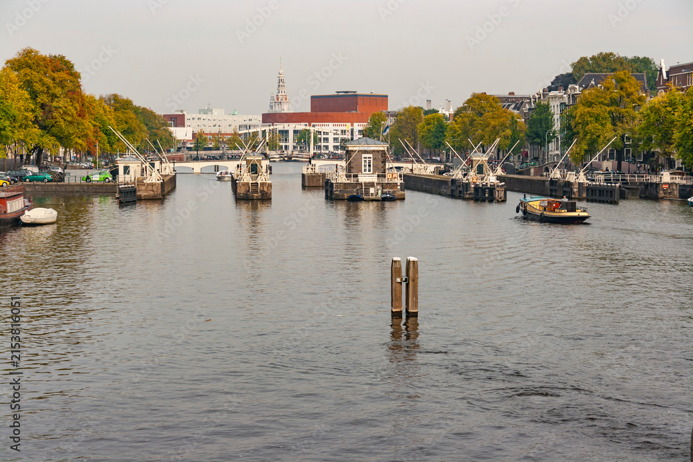 Fototapeta premium Scenic view of Amstel river with historic sluice gates, Magere Brug bridge and Stopera building in Amsterdam Netherlands