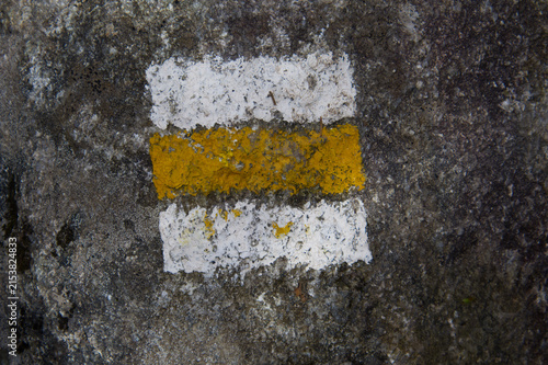 Konstfotografi Yellow and white painted tourist hiking trail sign marker on a rough stone surface