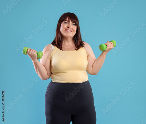 Cuadro en lienzo Overweight woman exercising with dumbbells on light blue background