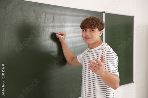 Fotografie Teenage boy writing on chalkboard in classroom