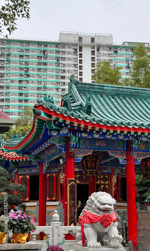 serene chinese temple in urban setting with lion statue foreground, stationary scene, red and green colors, stone and metal materials, clean and bright atmosphere, editorial and educational.