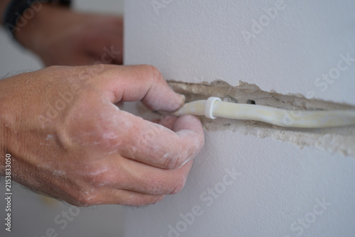 Bild auf Leinwand Hand placing cable conduit into channel cut in wall