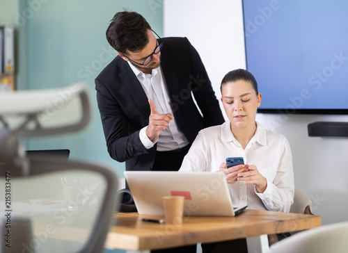 Quadro su tela Male boss chastises girl subordinate for idleness and scrolling of phone, social networks, snooze working time away