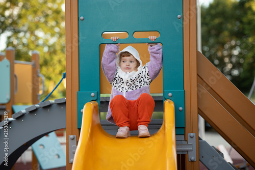 Bild auf Leinwand Child sitting at the top of a playground slide with adult supervision