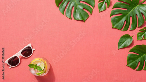 Buenos días summer drink with sunglasses and monstera leaves on coral