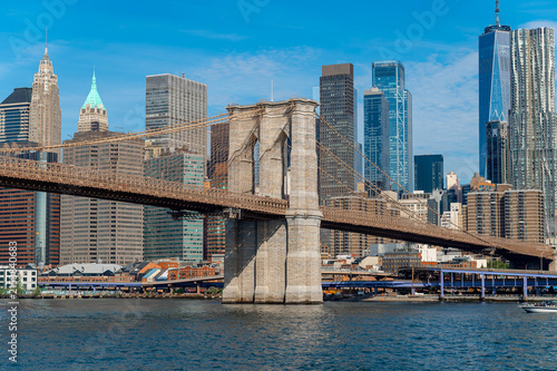 Brooklyn bridge and Manhattan skyline reflected over East river. Brooklyn Bridge tower, suspension cables, Manhattan skyscrapers and small boat on East River