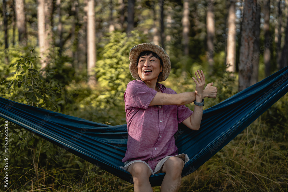 Fototapeta premium Woman enjoying nature while stretching in forest hammock