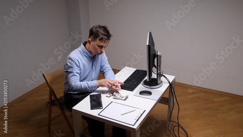 Foto Man sitting at a desk counting coins and crumpled cash, managing limited persona