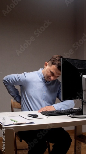 Obraz na płótnie Man in a business shirt sitting at a computer desk, experiencing lower back pain