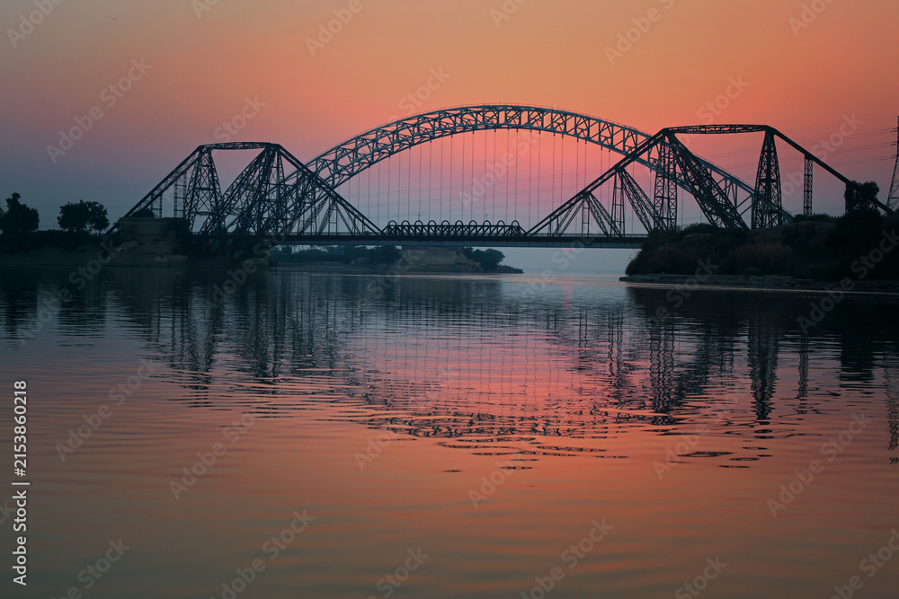 Fototapeta premium FPV aerial view of Ayub Bridge over the Indus River at sunset in Sukkur, Sindh, Pakistan.
