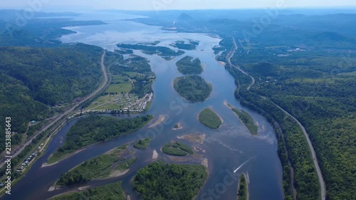 High‑altitude drone view of the Restigouche River estuary near a campsite, showing a boat navigating lush islands and channels dividing Quebec and New Brunswick.