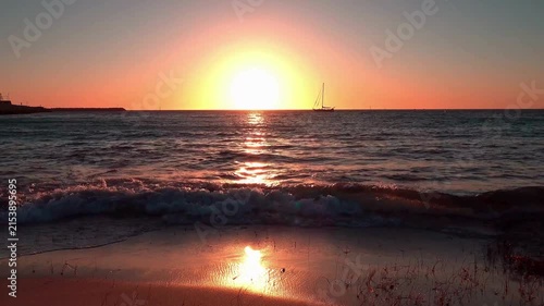 Sailboat Silhouetted Against Vibrant Orange Sunset Over Calm Ocean Waves 4k Video Footage Capturing Serene Coastal Horizon and Reflective Golden Hour Light