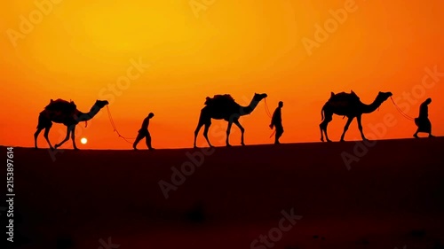 Silhouette of Nomadic Caravan Crossing Sahara Desert Dunes at Sunset 4K Footage Cinematic Travel Concept Featuring Bedouin Men and Camels Walking Slowly Across Golden Sand Landscape