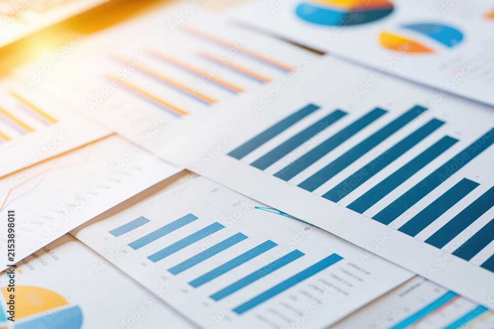 Fototapeta premium Colorful statistical charts and graphs printed on white paper sheets displaying data analysis results with blue orange and yellow tones