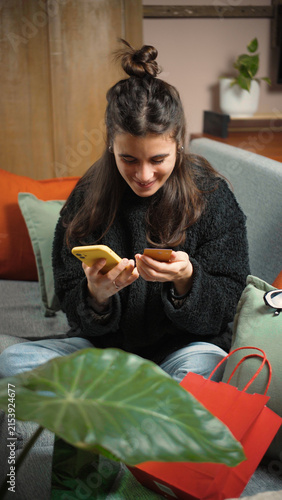 Young Latina woman sitting on her sofa shopping online with her payment card, browsing products and completing a purchase from home.