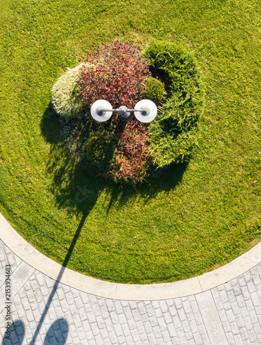 Aerial view of a lamp post with two spherical lights surrounded by lush green bushes and autumn foliage, creating a pareidolia effect resembling a face in an urban landscape in Belgrade, Serbia.