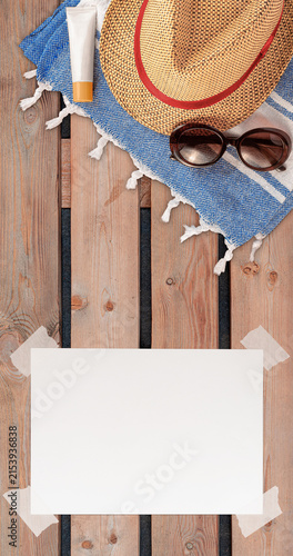 Summer Wallpaper with Straw Hat, Towel, Sunglasses, Protection Cream and White Blank Free Space Paper Sheet with Adhesive Tape on Wooden Surface. File with Clipping Path.